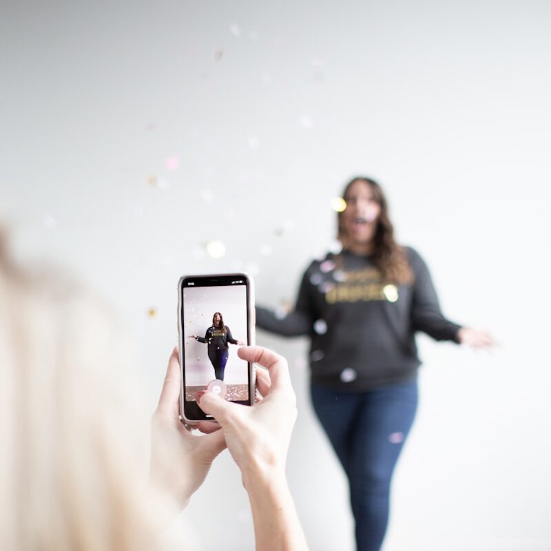 person holding white smartphone taking photo of woman wearing blue jeans